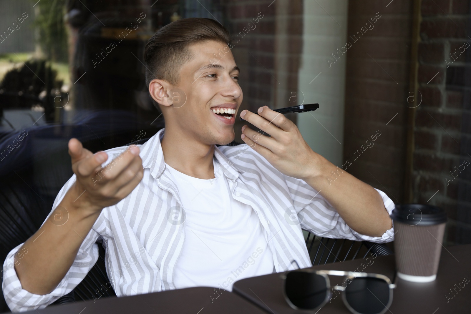 Photo of Young man recording voice message via smartphone in outdoor cafe