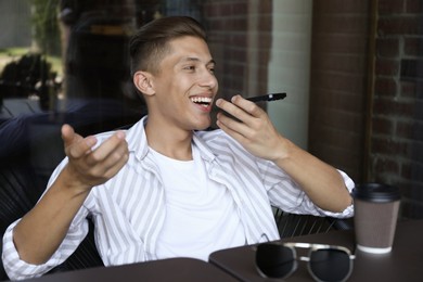 Young man recording voice message via smartphone in outdoor cafe