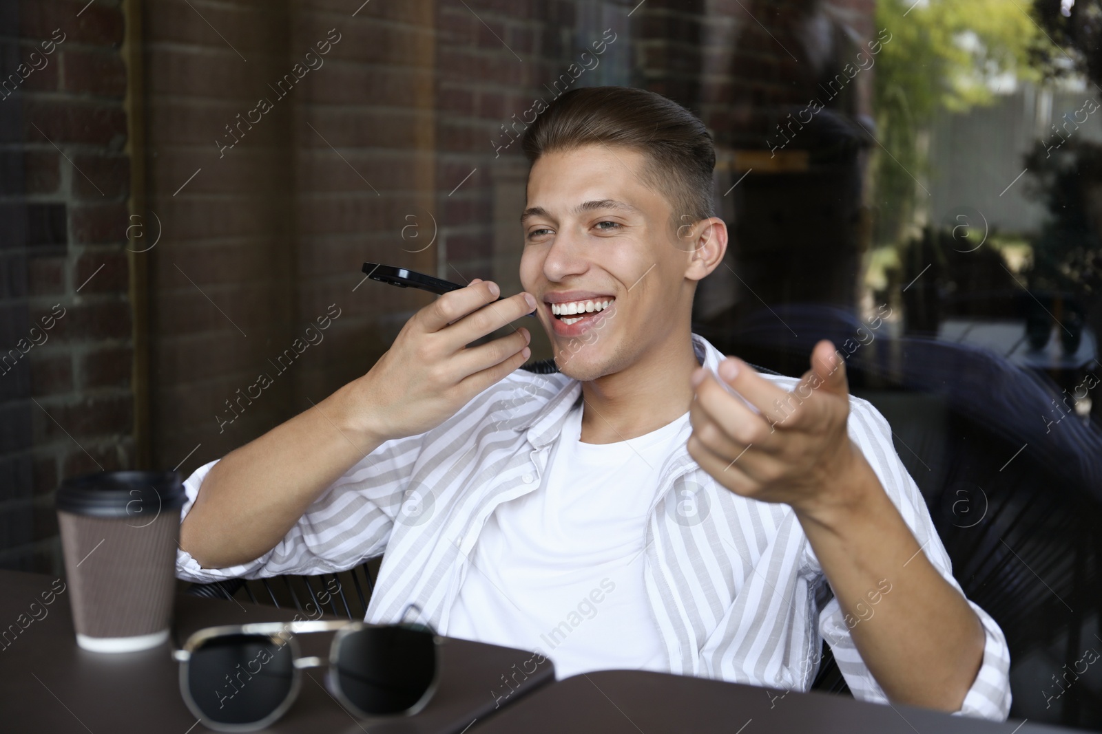 Photo of Young man recording voice message via smartphone in outdoor cafe