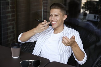 Young man recording voice message via smartphone in outdoor cafe