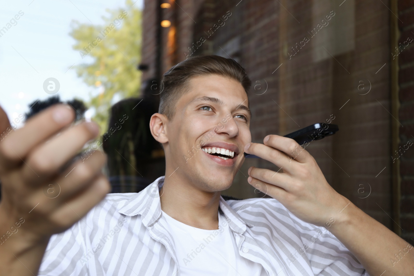 Photo of Young man recording voice message via smartphone outdoors