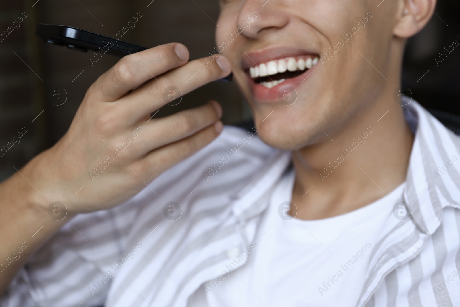 Photo of Young man recording voice message via smartphone outdoors, closeup