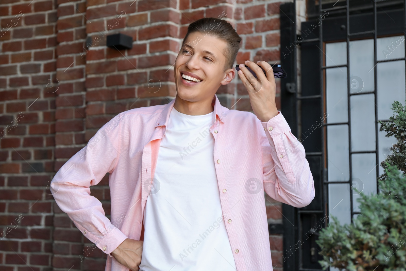 Photo of Young man with smartphone listening to voice message outdoors