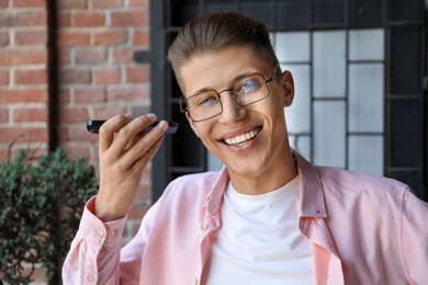 Young man with smartphone listening to voice message outdoors