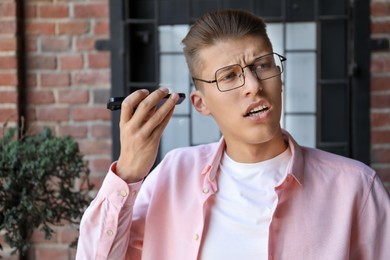 Young man with smartphone listening to voice message outdoors