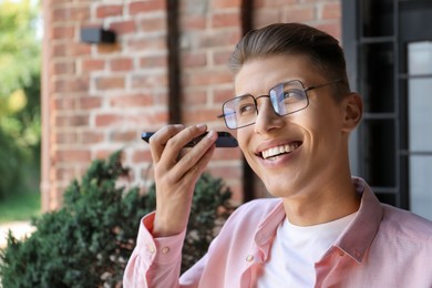 Young man with smartphone listening to voice message outdoors