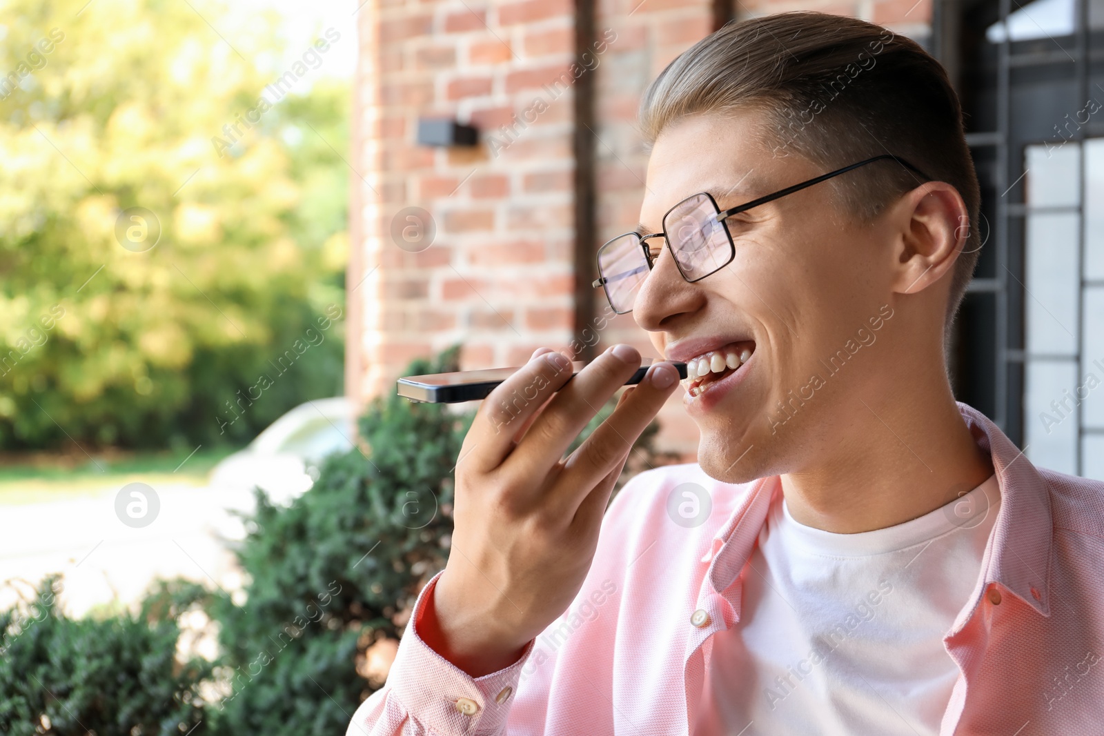 Photo of Young man recording voice message via smartphone outdoors