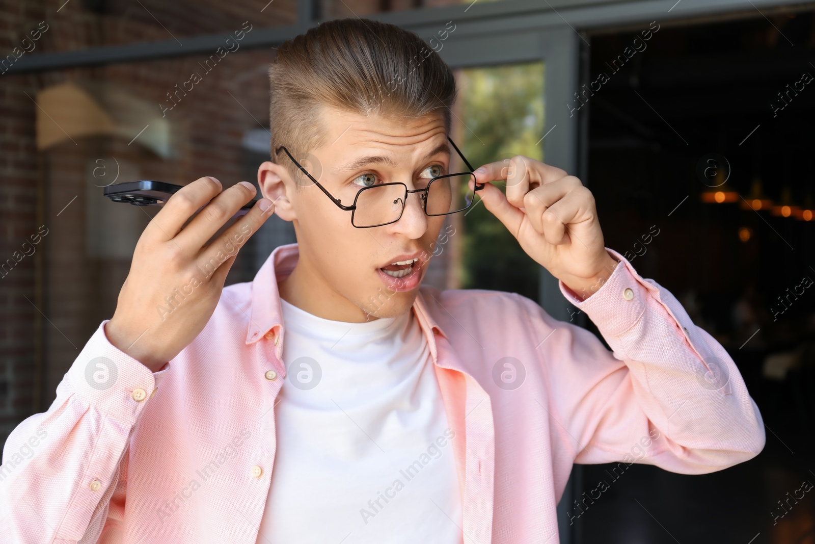 Photo of Young man with smartphone listening to voice message outdoors