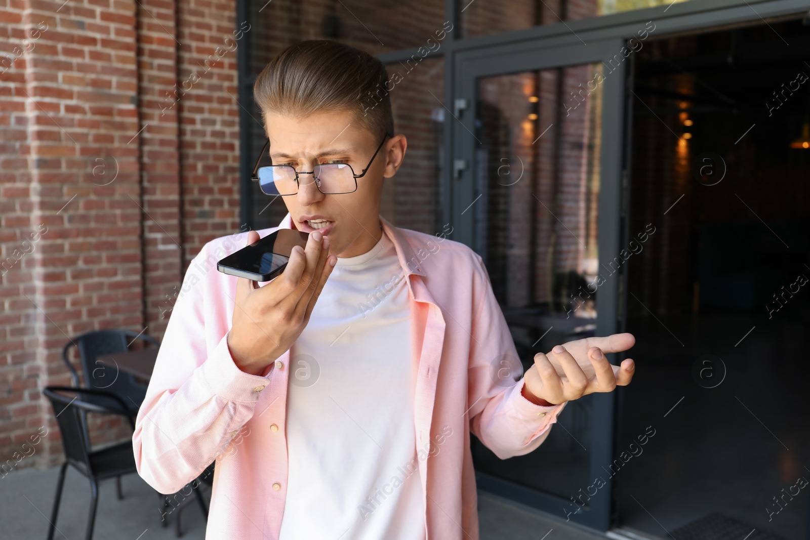 Photo of Young man recording voice message via smartphone outdoors