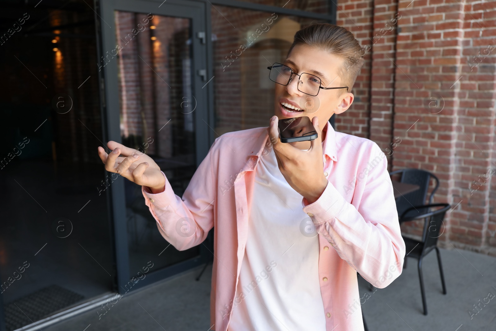 Photo of Young man recording voice message via smartphone outdoors