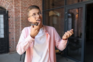 Young man recording voice message via smartphone outdoors