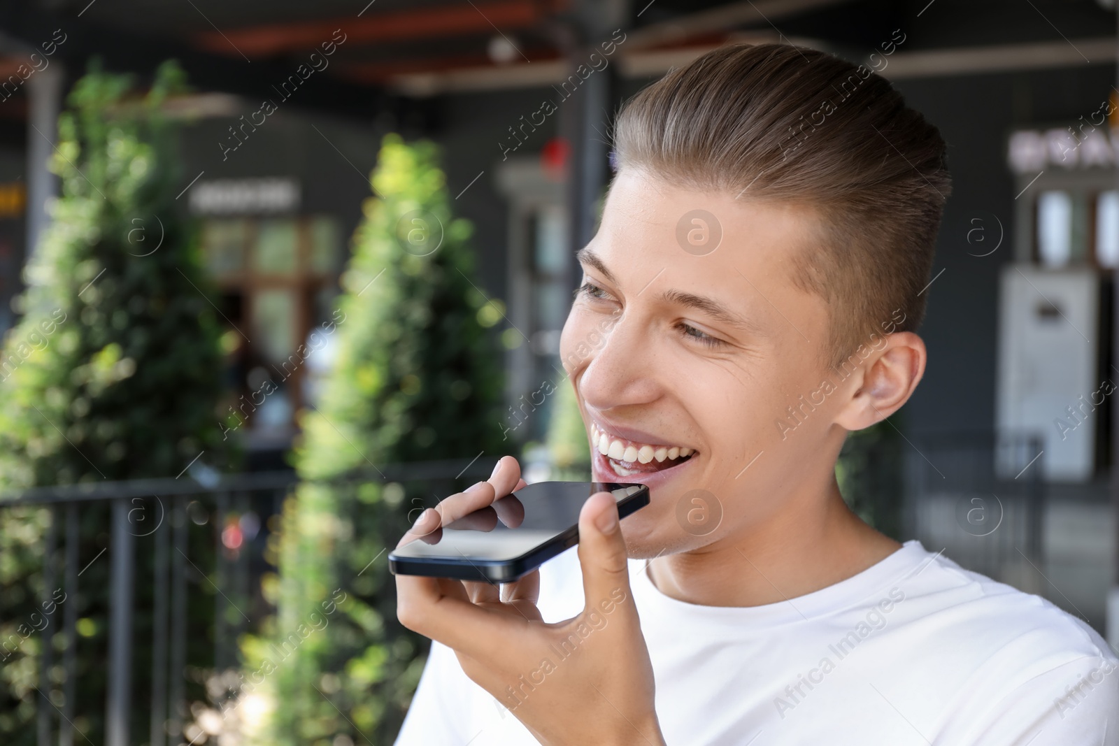 Photo of Young man recording voice message via smartphone outdoors