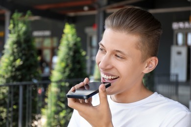 Young man recording voice message via smartphone outdoors