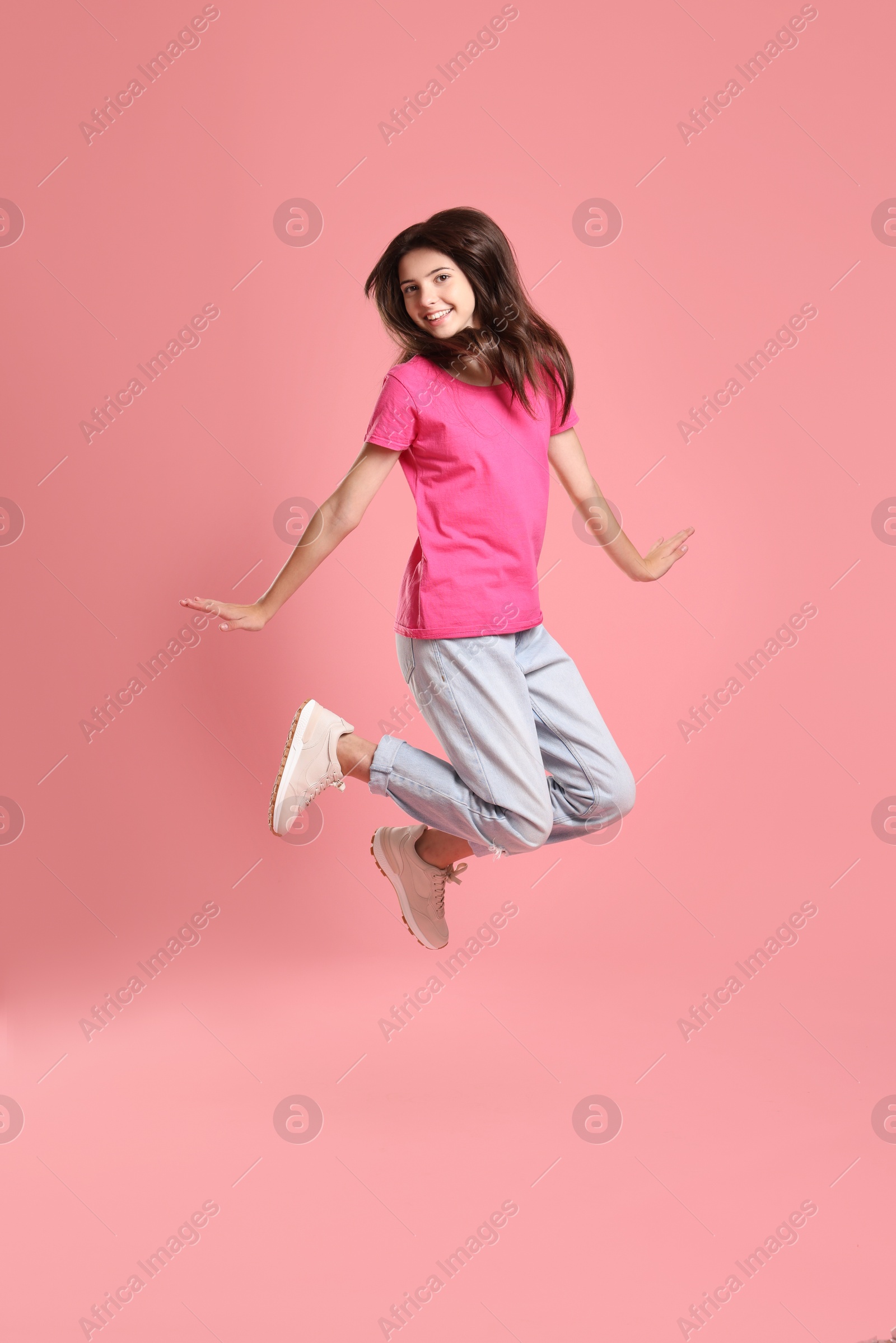 Photo of Happy teenage girl jumping on pink background