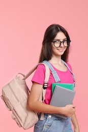 Portrait of cute teenage girl with backpack and books on pink background