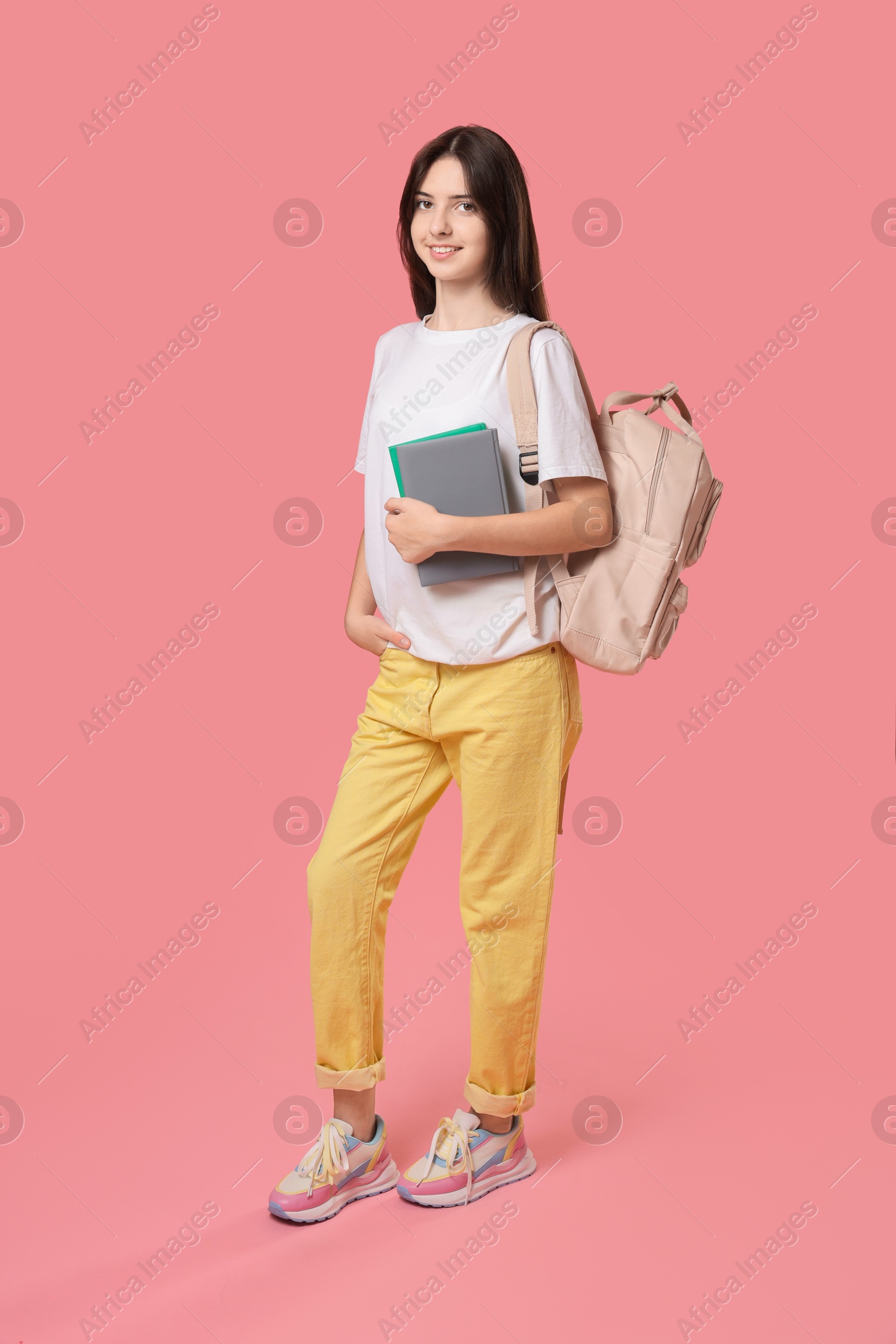 Photo of Cute teenage girl with backpack and books on pink background