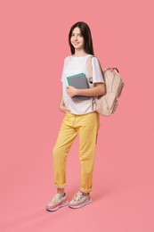 Cute teenage girl with backpack and books on pink background