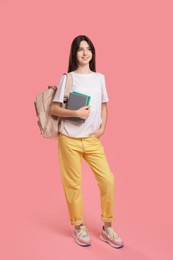 Cute teenage girl with backpack and books on pink background