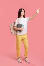 Photo of Cute teenage girl with backpack and books on pink background