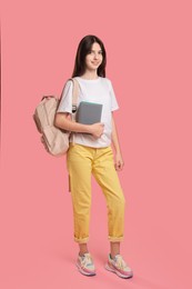 Cute teenage girl with backpack and books on pink background