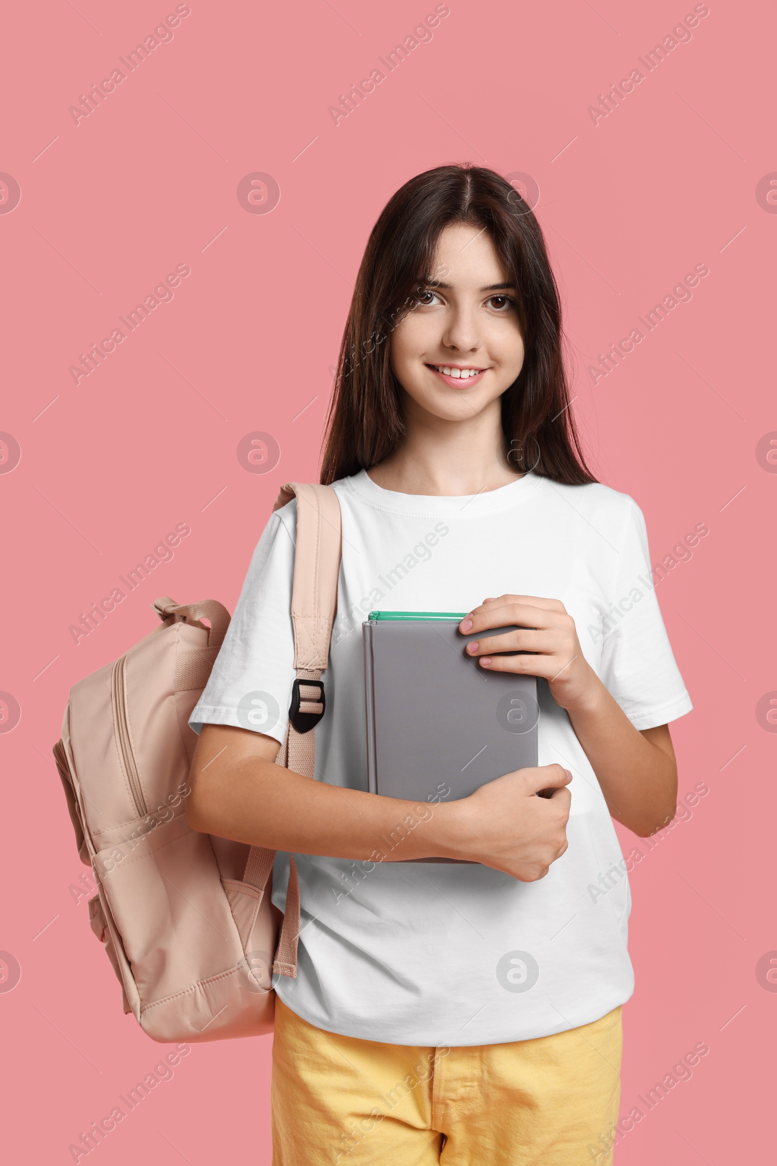 Photo of Portrait of cute teenage girl with backpack and books on pink background