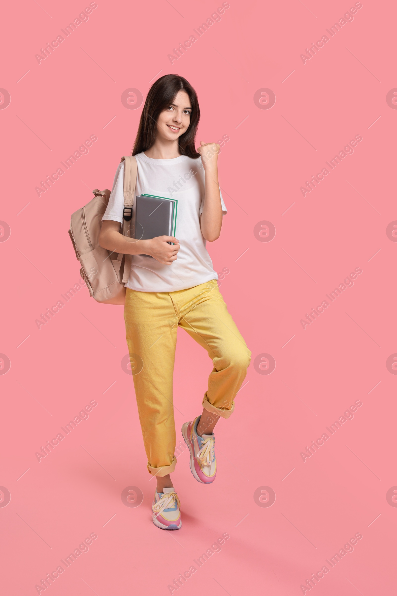 Photo of Cute teenage girl with backpack and books on pink background