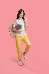 Cute teenage girl with backpack and books on pink background