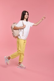 Cute teenage girl with backpack and books on pink background