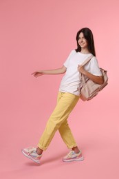 Cheerful teenage girl with backpack on pink background