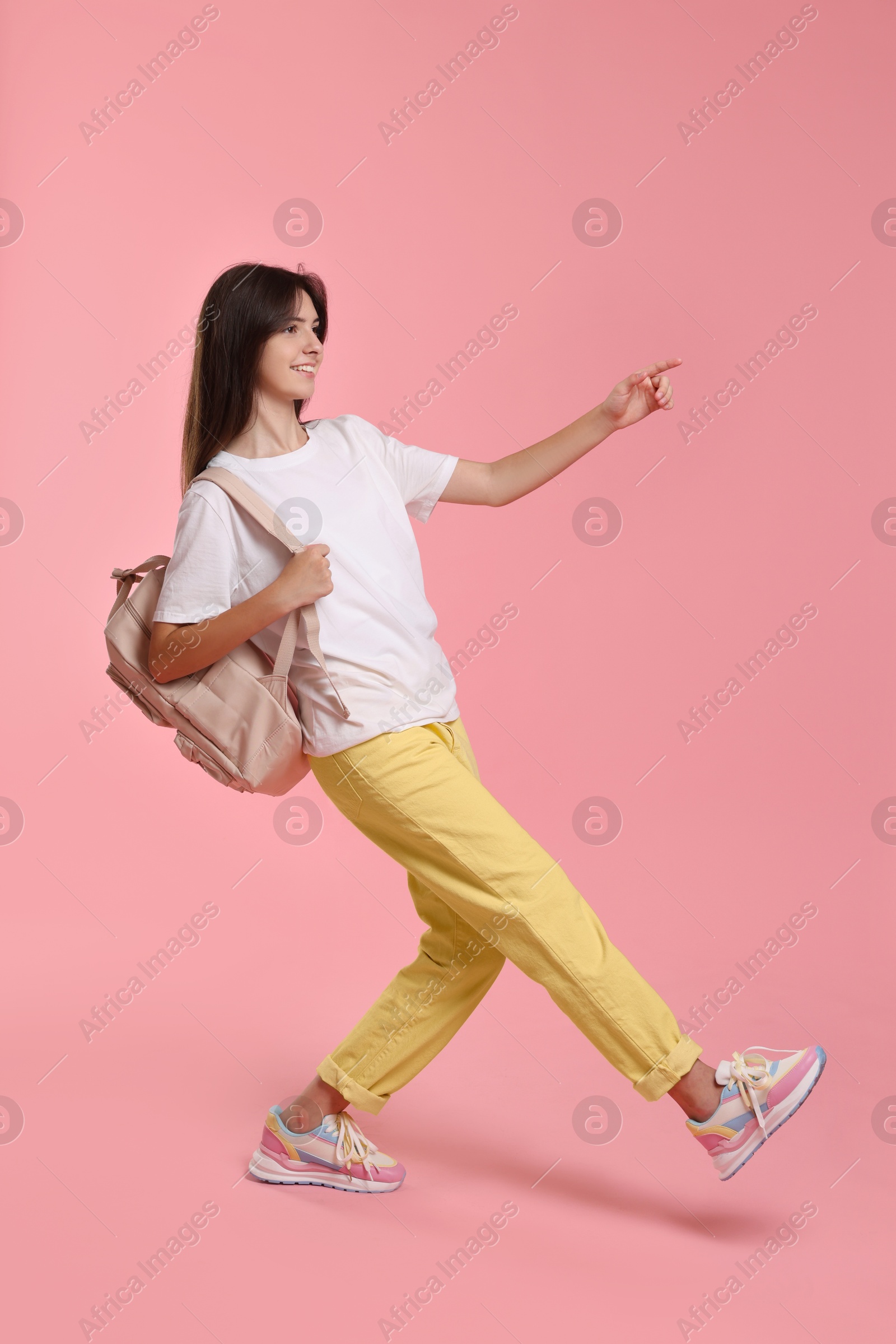 Photo of Cheerful teenage girl with backpack on pink background