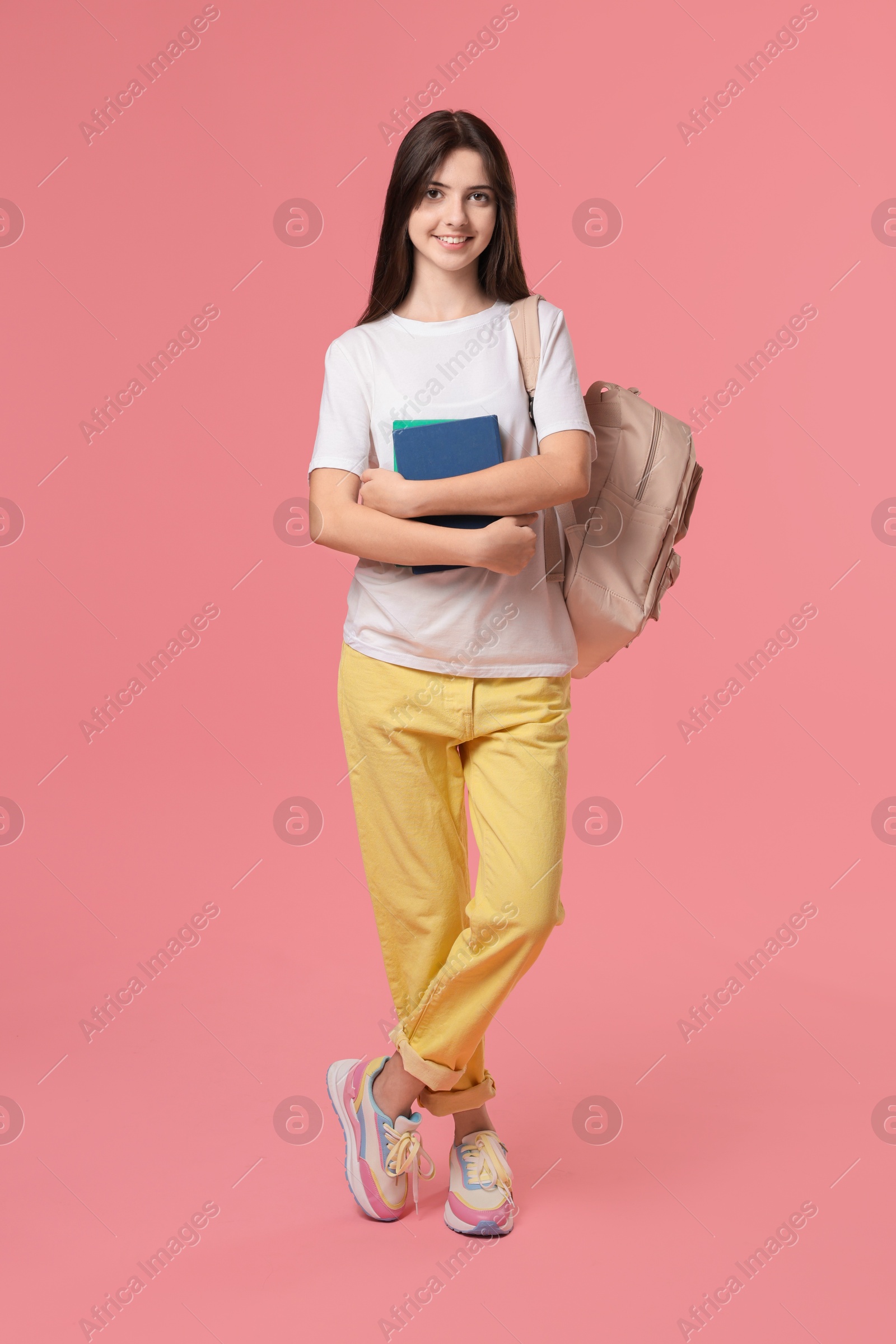 Photo of Cute teenage girl with backpack and books on pink background