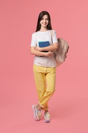 Cute teenage girl with backpack and books on pink background