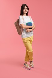 Cute teenage girl with backpack and books on pink background