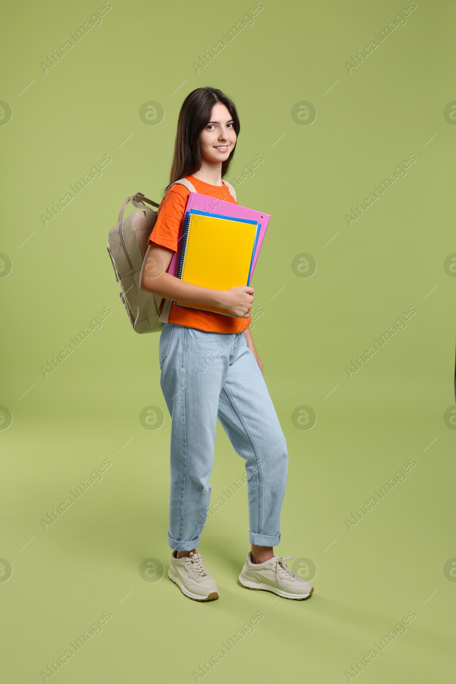 Photo of Cute teenage girl with backpack and books on olive background