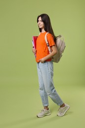 Cute teenage girl with backpack and books on olive background