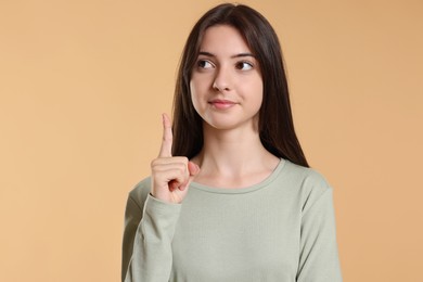 Portrait of cute teenage girl pointing at something on beige background