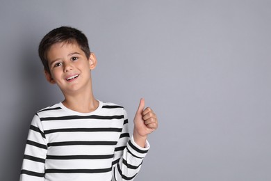 Cute little boy showing thumbs up on grey background, space for text