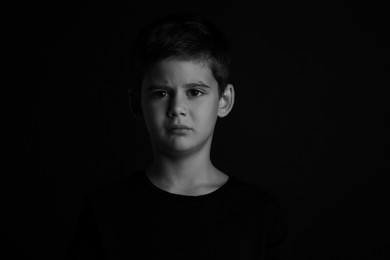 Photo of Portrait of sad little boy on dark background. Black and white effect