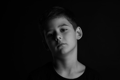 Portrait of sad little boy on dark background. Black and white effect