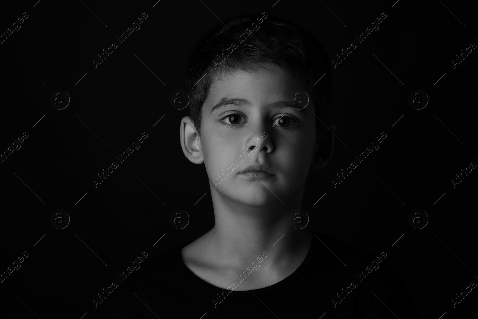 Photo of Portrait of sad little boy on dark background. Black and white effect