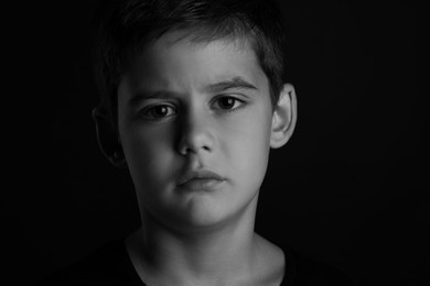 Photo of Portrait of sad little boy on dark background. Black and white effect