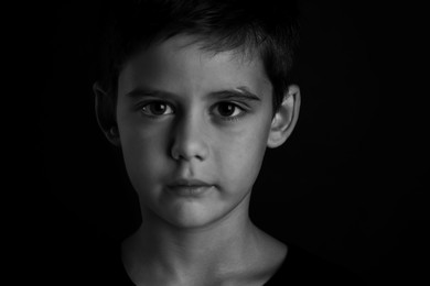 Photo of Portrait of sad little boy on dark background. Black and white effect