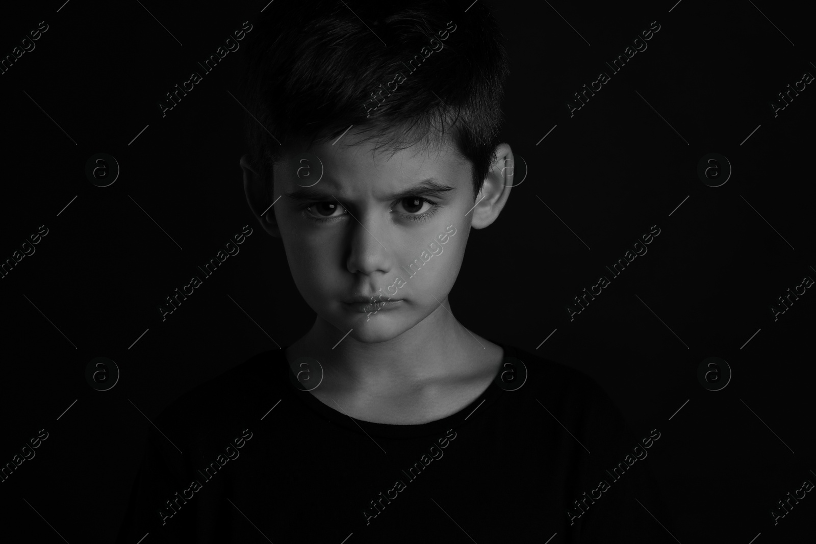 Photo of Angry little boy on dark background. Black and white effect