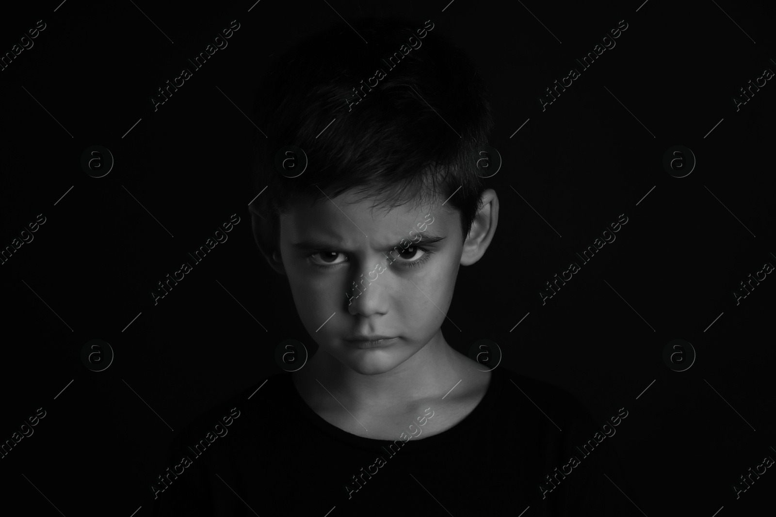 Photo of Angry little boy on dark background. Black and white effect