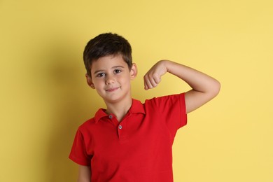 Photo of Cute little boy showing his bicep on yellow background