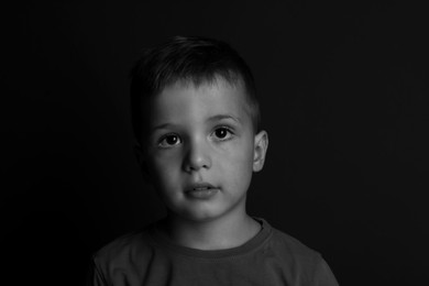 Photo of Portrait of sad little boy on dark background. Black and white effect