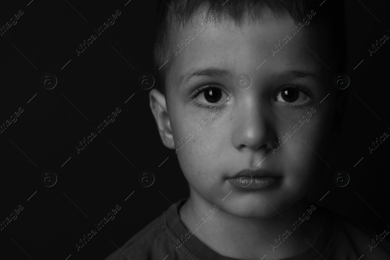 Photo of Portrait of sad little boy on dark background, space for text. Black and white effect