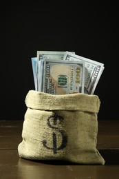 Photo of Dollar banknotes in sack on wooden table against dark background