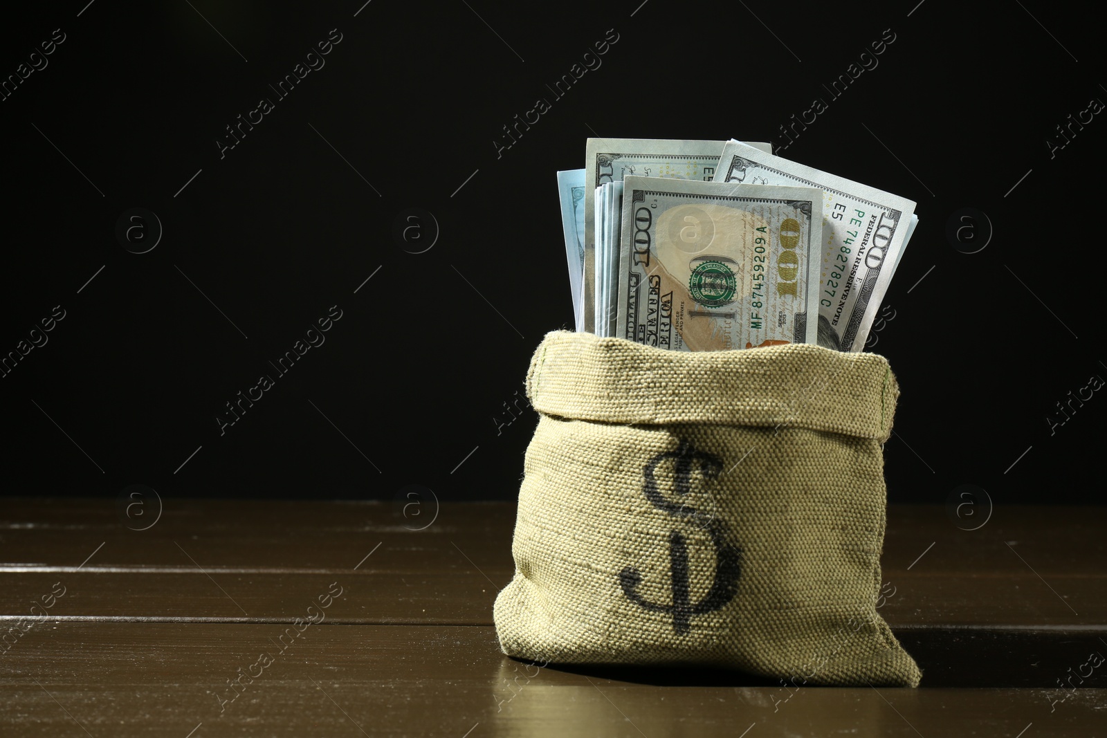 Photo of Dollar banknotes in sack on wooden table against dark background, space for text