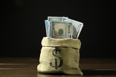 Photo of Dollar banknotes in sack on wooden table against dark background